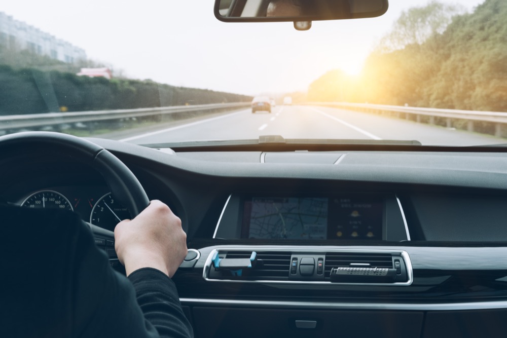 Driver holding the steering wheel on a highway with a sunrise in the background