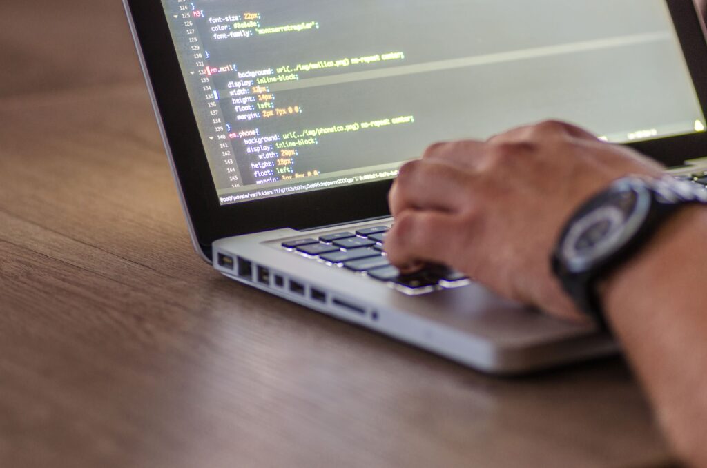 Hands using a laptop displaying code on its screen.